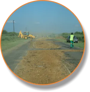 Backhoe loader grading a dusty road with a worker standing by