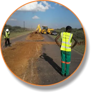 Team member in a high-visibility vest beside a backhoe loader on a road
