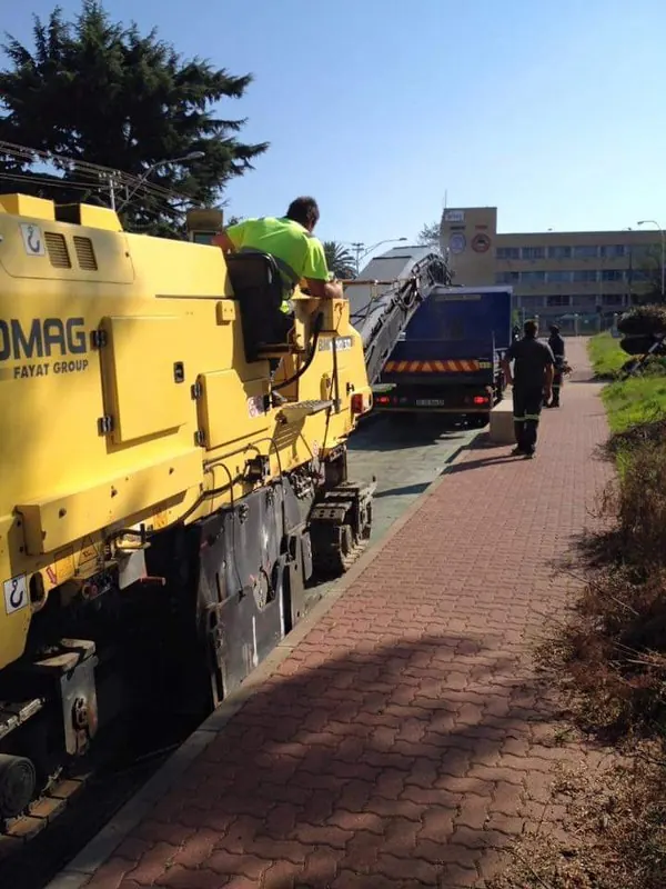 Milling machine loading a truck beside a paved walkway